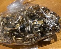 Plastic bag containing a large number of metal cuff links in gold and silver tones with different designs.