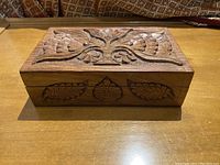Top angled view of rectangular carved wooden box showing flower and leaf designs on lid and front panel.