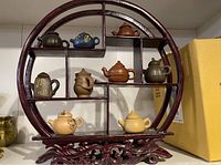 Full front view of the circular wooden shelf holding eight miniature teapots in various colors and styles.