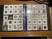Open binder pages showing assorted world coins organized in plastic sleeves with labels for Chile and other countries.