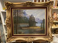 Full view of the framed oil painting showing mountain lake landscape with detailed ornate gold and red frame.