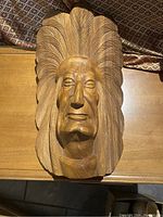Front view of carved wooden Indigenous chief head wall hanging with feather details and facial features.