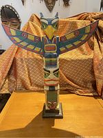 Full front view of the carved indigenous wooden totem pole with wings extended, showing colorful paint and detailed carving.