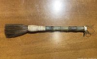 Full view of the calligraphy brush showing jade and bone handle with dark bristles.
