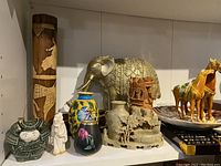 Wide view of multiple Asian decorative items including figurines, vases, brass elephant, and wooden carvings arranged on shelf.