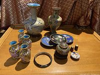 Full view of all cloisonné items arranged on a wooden table, showing two large vases, five smaller vases, three small dishes, bracelet, covered jar, and two small snuff bottles.