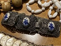 Close-up of filigree bracelet with three blue and white porcelain insets, white bead necklace, and wooden bead necklace on a wooden surface