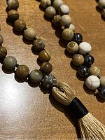 Close-up of the round stone beads showing natural colors and the decorative silver-tone bead and cream tassel with black wrap.