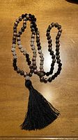 Full view of the mala necklace showing the arrangement of black, pink, and light grey stone beads and the large black tassel hanging from one end.