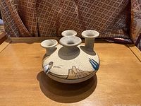 Front view of Navajo stoneware vase with four flared spouts and hand-painted desert landscape including mesas and figures.