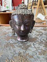 Front-right angle showing facial details and overall shape of the bronze Buddha head on patterned fabric.