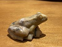 Side view of a small stone frog sculpture with natural veining and smooth polished surface.