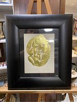 Full view of the framed artwork, showing the black wide frame and the gold embossed image of 'The Bear Mother'.