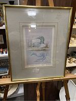 Full view of the framed art print sitting on a wooden easel showing the whole piece and frame.