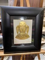Full view of framed artwork showing black wooden frame and gold embossed raven print.