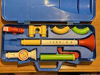 Blue plastic carrying case with molded interior slots holding multiple colorful plastic toy instrument parts