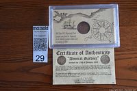 Shipwreck coin mounted in a display holder with vintage nautical illustrations and certificate of authenticity placed below.