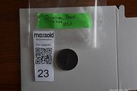 The Québec Bank 1852 token coin inside a clear plastic bag with a green label identifying it.