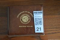 Brown leather case showing gold embossed text and emblem: 'Crossroads of the World Gander Aviation Dollar'