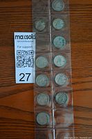 Photo shows a collection of 11 Canadian silver dimes in a transparent coin holder sleeve, laid flat on a wooden surface next to a maxsold auction lot number card.
