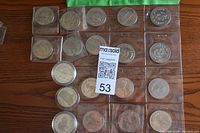 Top view of multiple Canadian trade dollars arranged in plastic holders on a wooden surface. Coins vary in design and depict different themes and events.