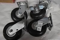 Four new heavy duty casters with black rubber wheels and metal mounting plates, arranged together on a white surface.