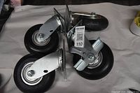 Four heavy duty casters shown on a flat surface, three without locks and one with a wheel lock and grease fittings