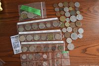Photo showing variety of foreign coins arranged in plastic holders with dates labeled, plus loose coins laid on table.