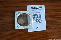 Larger photo of the Newfoundland 10 cents 1944 coin in holder alongside the auction lot number 4 card seen on wooden surface.