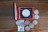 Silver dollar coin commemorating RCMP 1873-1973 in a red velvet collector case with eight matching 25-cent quarters spread below on a wooden surface.