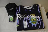 Full view of the Rick and Morty large sweatshirt folded with a black ball cap and boxed playing cards placed beside it.