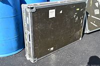 Wide angled image showing exterior of large black road case with scuffs and scratches against blue barrels.