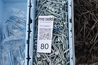 Close-up photo showing silver Phillips head screws and black coated screws packed in trays, with small bagged screws in separate plastic bags.