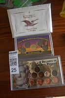 Photo showing unopened white envelope from The American Historic Society labeled 'Genuine Coin Collection', Wild West Coin Collection card with three coins, and a set of coins titled '9 Decades of Lincoln Pennies' inside a clear plastic holder
