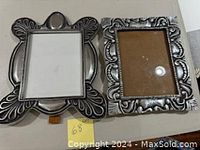 Two large pewter picture frames displayed side by side showing detailed decorative metalwork.