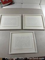 Three framed black and white abstract line drawings arranged on a surface. Each enclosed in a white frame with a white mat.