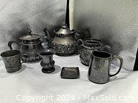 Full view of 7 antique metal serving pieces including teapot, sugar holders, toothpick holder, vanity tray, and cups showing metal alloy finish and initial engravings.