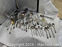 Wide view of 48 antique silverware pieces including forks, knives, spoons, spoons, serving pieces laid out on a white surface