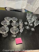 View of all glassware including 4 nude male-shaped shot glasses, 6 etched crystal wine glasses, and 4 additional etched crystal glasses (2 short wine, 2 tall water) arranged on table.