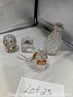 Four glass items: cut glass decanter, small square crystal box with spoon, tiny painted glass, and small crystal-amber pot.