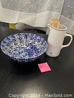 Wide shot showing the blue and white ceramic mixing bowl next to the tall white ceramic pitcher with wooden utensils inside.