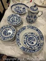 Multiple blue and white porcelain side dishes and large dinner plates with floral designs, laid out on white sheet.