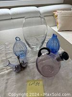 All items in the lot displayed together on a flat surface: large clear glass vase, two small blue vases, purple teapot glass vase, and purple antique glass bottle set with metal handle.