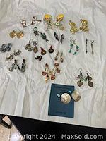 Multiple sets of mixed costume pierced earrings displayed on white surface, various styles and colors visible