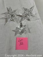 Three crystal star shaped items on white fabric: one smaller star paperweight and two larger star candle stick holders