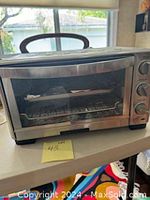 Full view of stainless steel Cuisinart toaster oven on a table showing front door and control knobs.