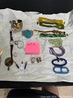 Full lot showing bracelets, rings, watches, charms, bookmark, and hand mirror laid on white paper.