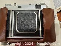 Front of Kodak Retina II camera in brown leather case showing Kodak logo on black textured front panel