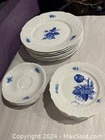 Stack of white porcelain plates and saucers with blue floral rose design, showing the embossed rim detail.
