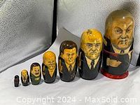 Seven wooden Russian nesting dolls painted as past Russian leaders displayed in a row from largest to smallest.